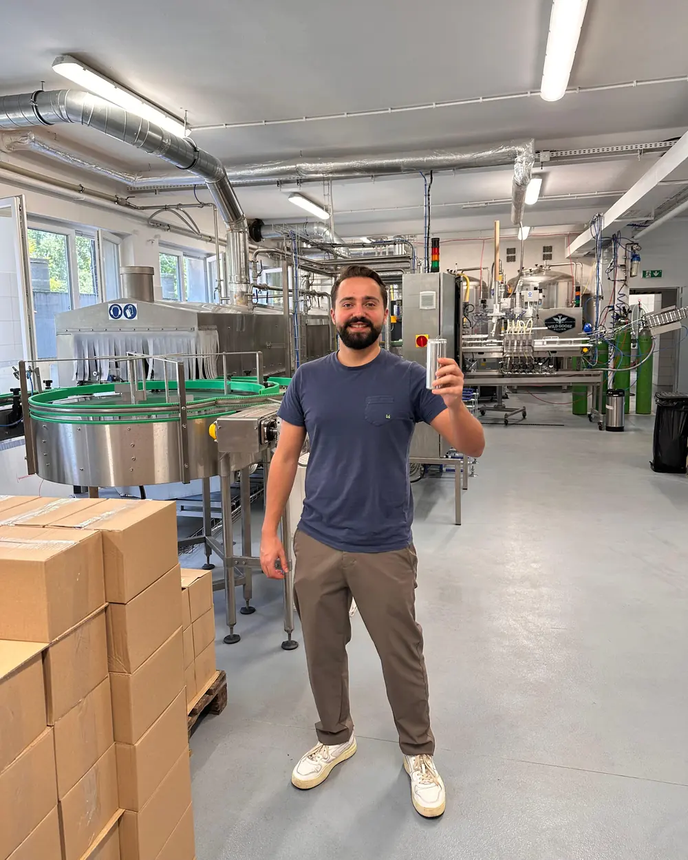 Timur El Ait on a beverage production floor, holding up a can