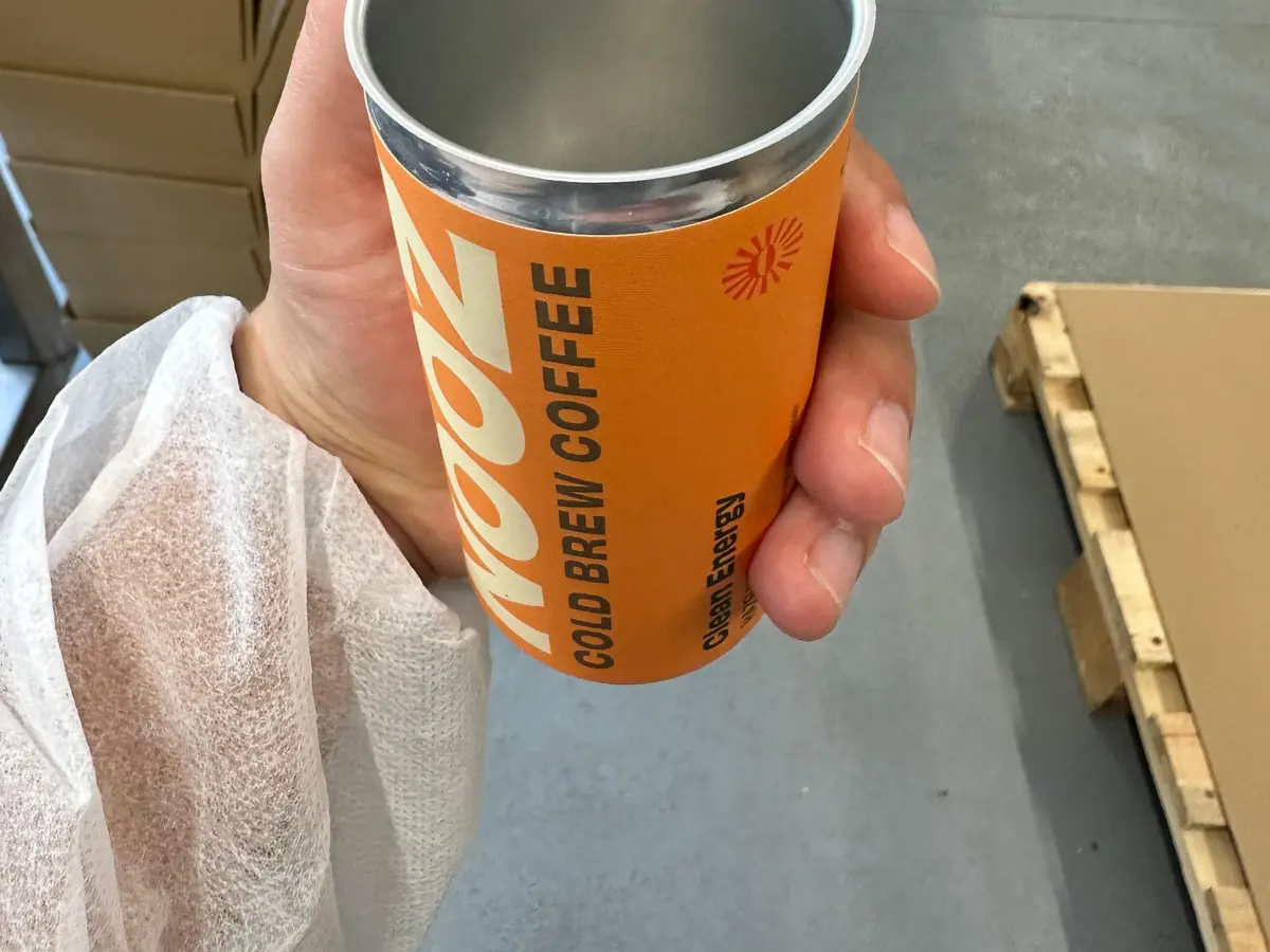 A NOOZ cold-brew coffee can held up on the production floor