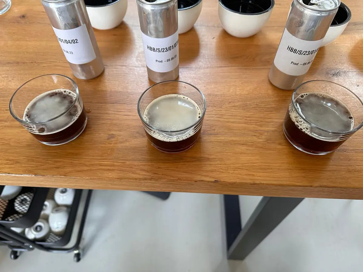 Three cold-brew samples in glasses on a tasting table, each in front of its labelled sample can